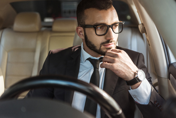 handsome pensive driver sitting in car and looking away - Foto, imagen