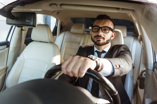 cheerful handsome driver in suit and glasses driving car - Foto, imagen