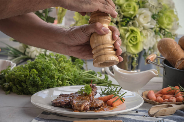 Male hands serving lamb steak on white plate. - Φωτογραφία, εικόνα