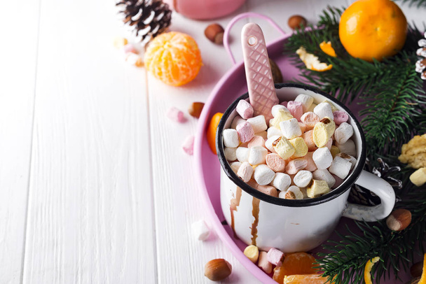 two cups with hot chocolate or cocoa with melted marshmallow, pina cone, spruce branches and mandarin on tray on white wooden background - Zdjęcie, obraz