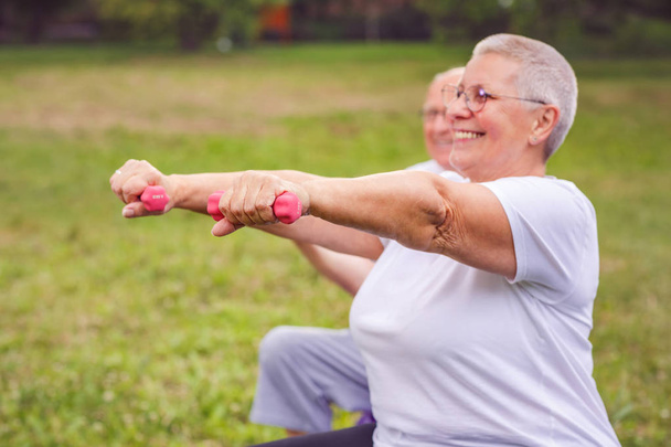 Kurzhanteln in Nahaufnahme lächelnde Seniorin sitzt mit Hantel auf Fitnessball - Foto, Bild