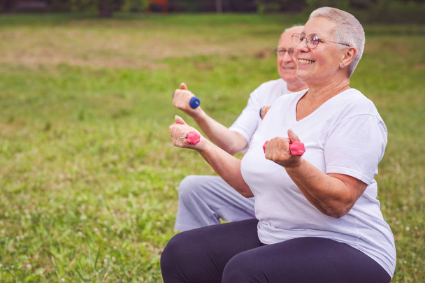 Sonriente mujer deportiva senior sentada en la pelota de fitness con mancuerna
 - Foto, Imagen