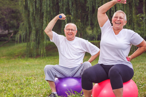 Coppia di anziani che solleva i manubri mentre si siede sulla palla fitness nel parco
 - Foto, immagini