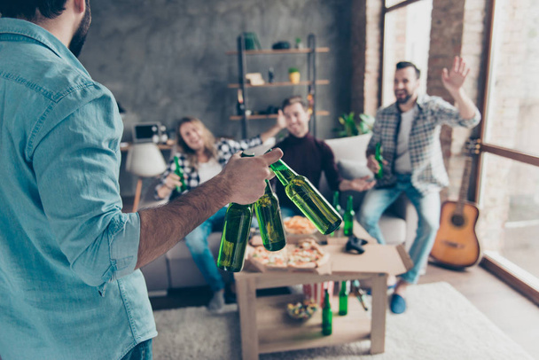 Cropped rear view of visitor bringing bottles with beer to his stylish, successful, attractive friends  who extremely happy, glad to see him with raised palm gesturing on blurred background - Foto, Imagem