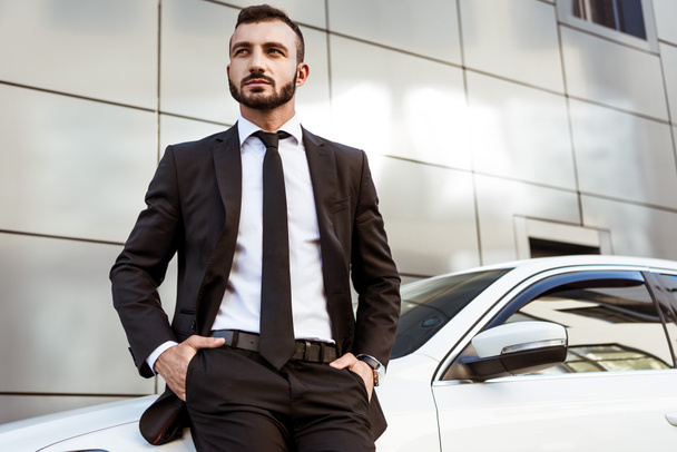 handsome businessman leaning on car and looking away - Фото, зображення