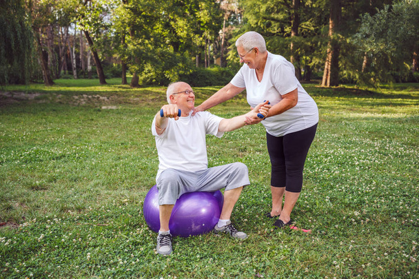 Lachende volwassen man en vrouw samen doen van fitness oefeningen op fitness bal in park Concept van gezonde levensstijl - Foto, afbeelding