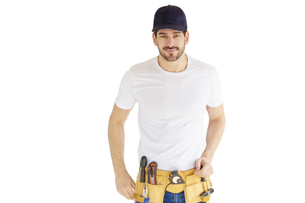 Portrait of handsome young handyman wearing baseball cap and tool belt while standing at isolated white background with copy space. - Photo, image