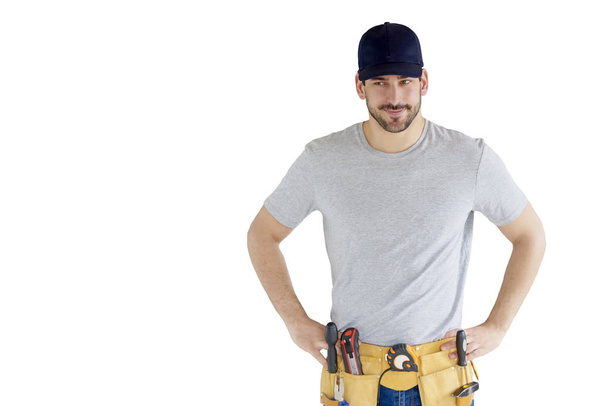 Portrait of handsome young handyman wearing baseball cap and tool belt while standing at isolated white background with copy space. - Фото, изображение