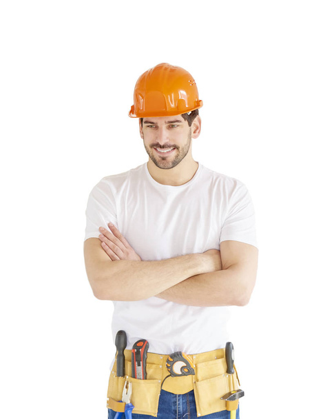 Portrait of young handyman wearing hard hat and tool belt while standing with arms crossed at isolated white background with copy space. - Valokuva, kuva