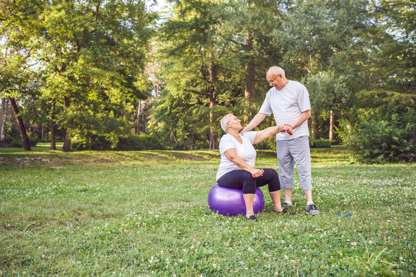 Concepto de estilo de vida saludable sénior - Feliz pareja de ancianos hacer ejercicio juntos en la pelota de fitness en el parque
 - Foto, imagen