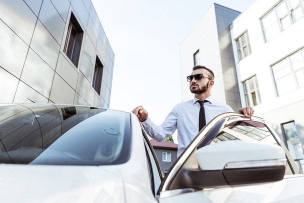 handsome driver in sunglasses standing near open car on street - Foto, Imagem