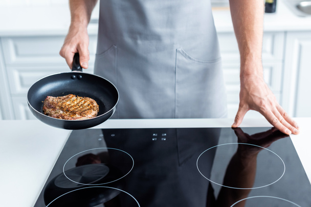 cropped shot of man in apron holding frying pan with delicious steak - 写真・画像