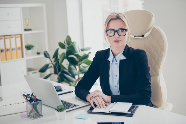 Porträt einer charmanten hübschen Frau mit Brille und moderner Frisur, die im weißen Büro sitzt und in die Kamera blickt - Foto, Bild