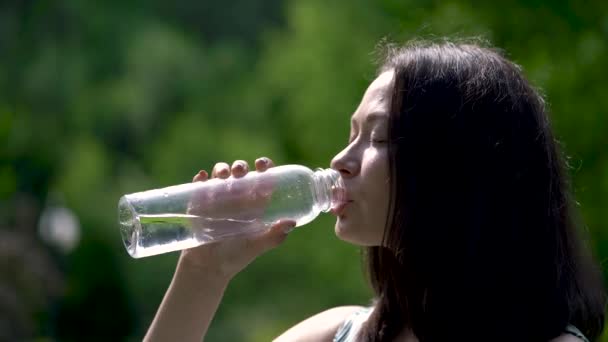 Κοντινό πλάνο, μια ευτυχής αναζητούν Ασιατικές γυναίκα ποτά νερού από ένα διαφανές μπουκάλι. Sunrays είναι στο πρόσωπό της. - Πλάνα, βίντεο
