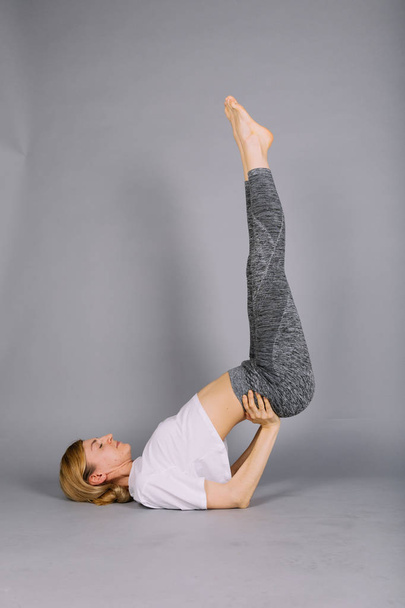 sportlich schöne junge Frau praktiziert Yoga, trainiert in grau-weißer Sportbekleidung, Studio, volle Länge - Foto, Bild
