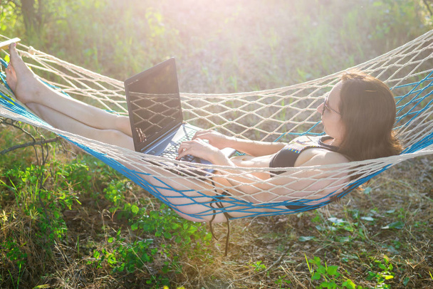 Mujer joven acostada en una hamaca y mirando a un portátil. Mujer adicta al trabajo trabajando en vacaciones, espacio
. - Foto, Imagen