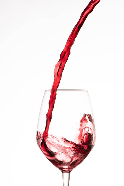 Κόκκινο κρασί ρίχνει σε ένα ποτήρι κρασί, σε λευκό φόντο - Φωτογραφία, εικόνα