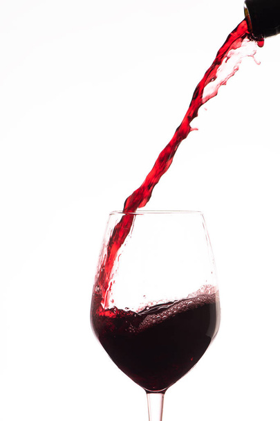Red wine pouring in a wine glass, on a white background - Photo, Image