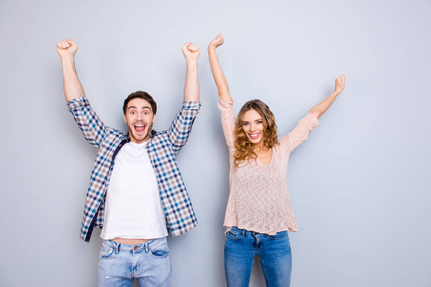 Portrait of stylish couple in casual outfits wearing jeans holding hands up celebrating achievement isolated on grey background - Фото, зображення