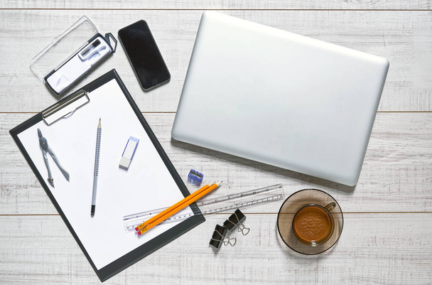 Ansicht eines Holztisches mit Laptop, Handy, Papier, Bleistift, Spitzer, Gummi, Clips, Bremssätteln, Lineal und einer Tasse Kaffee darauf - Foto, Bild