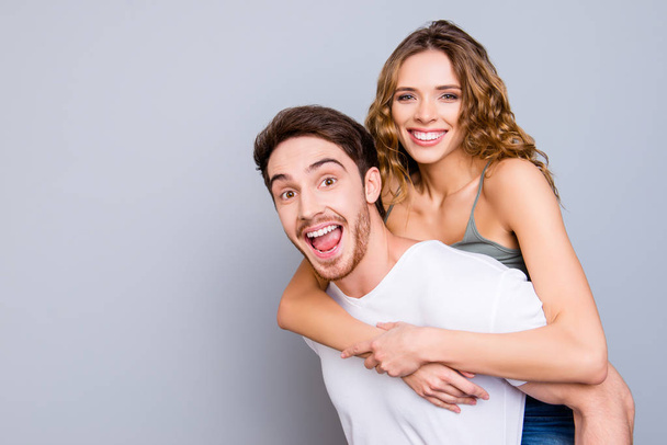 Portrait with copy space empty place of cheerful positive couple, amazed man carrying on back pretty toothy woman isolated on grey background. Advertisement concept - Foto, Imagem