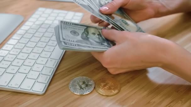 Female hands counting cash with bitcoins. Crop view of woman hands counting large bundle of dollar banknotes on wooden desk with bitcoins and keyboard. - Video
