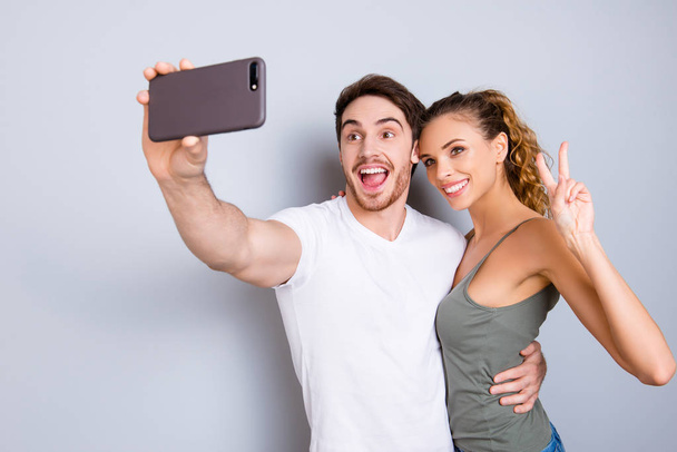 Online internet meeting technology apps gadget concept. Portrait of friendly peaceful couple shooting selfie on front camera gesturing v-sign with hand enjoying video-call - Foto, afbeelding