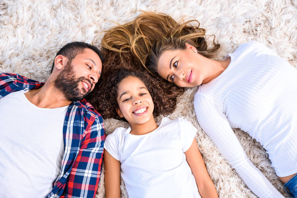 Young parents and their daughter laying on the carpet - Foto, imagen