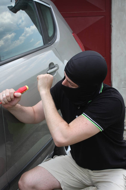 Ladrón de coches tratando de entrar en un coche con un destornillador
. - Foto, imagen
