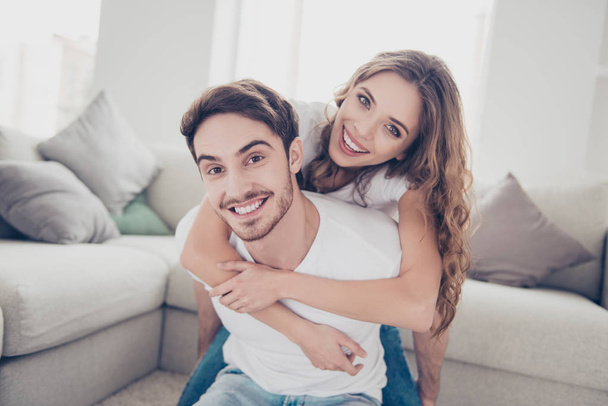 Portrait of cheerful positive spouses, man with bristle carrying on back charming woman with curly hair looking at camera enjoying time together indoor. Recreation weekend holiday concept - Фото, изображение