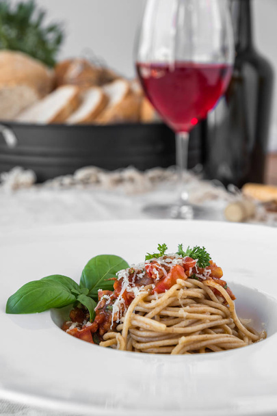 Delicious spaghetti topped with bolognaise sauce and basil served with red wine. - Foto, afbeelding