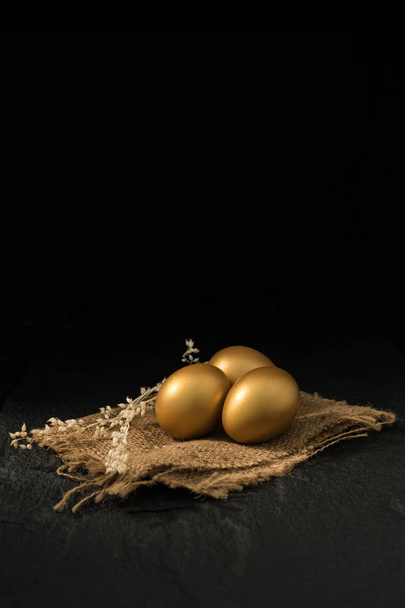 Golden eggs on sackcloth napkin on dark background. - 写真・画像