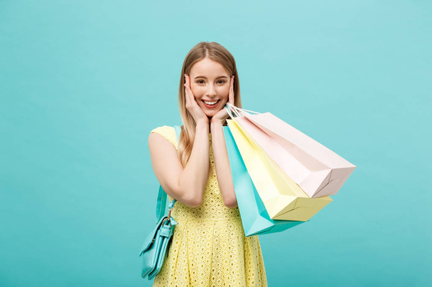 Alışveriş torbaları üzerinde mavi arka plan izole tutan sarı elbise heyecanlı bir güzel kız portresi. - Fotoğraf, Görsel