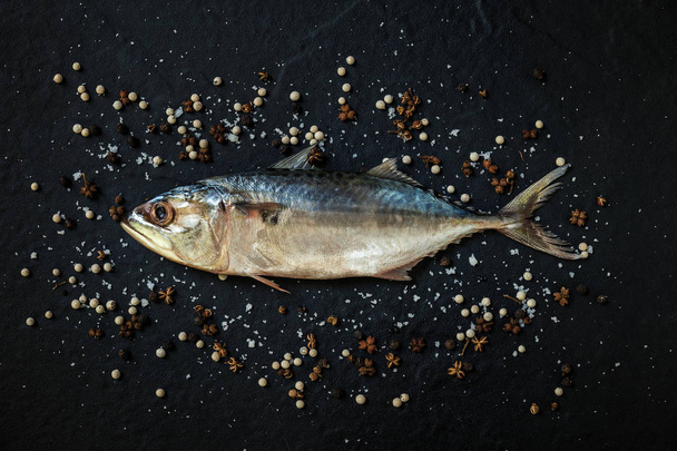 Top view of fresh, raw mackerel with sea salt and pepper on black background. - Foto, afbeelding
