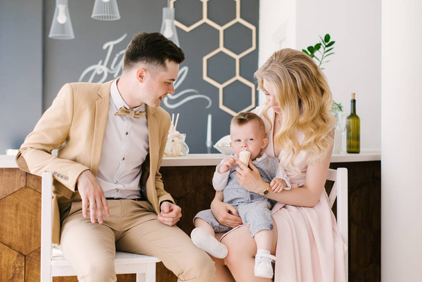 Beautiful young parents smile with their one-year-old child at home in a beautiful interior in pastel colors. Family look. Happy birthday party - Foto, Imagem
