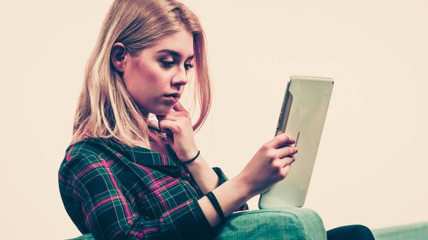 Young teenage woman using tablet while sitting on sofa and relaxing surfing on internet - Foto, Imagem