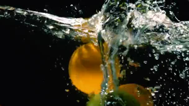 Fresh green apples and oranges fall into water with splash on a black background close-up slow motion - Filmagem, Vídeo