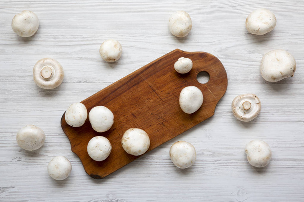 Cogumelos de champignon em tábua de madeira sobre superfície de madeira branca, vista superior. Por cima, por cima.
. - Foto, Imagem