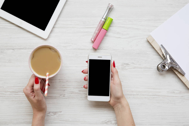 Espace de travail féminin avec tablette, bloc-notes, feuille, latte ice, smartphone et mains féminines sur une surface en bois blanc, vue de dessus
.  - Photo, image