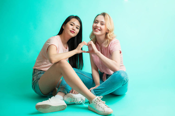 Young girls showing heart sign with their hands sitting over blue background - Φωτογραφία, εικόνα