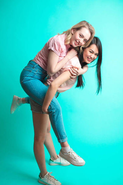 Two playful interacial girls piggybacking and having fun at studio - Fotó, kép
