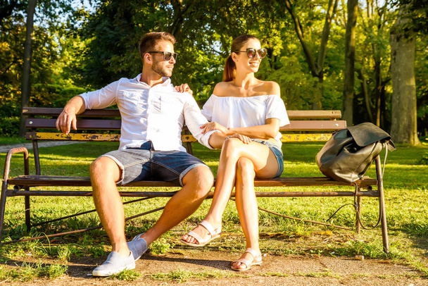 A beautiful young couple sitting on a bench in a park in the sunset - Valokuva, kuva