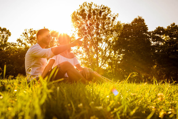 Piękna Młoda para siedzi na boisko w parku w zachodzie słońca - Zdjęcie, obraz