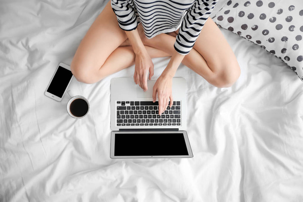 Female blogger with laptop and cup of coffee on bed, top view - Фото, зображення