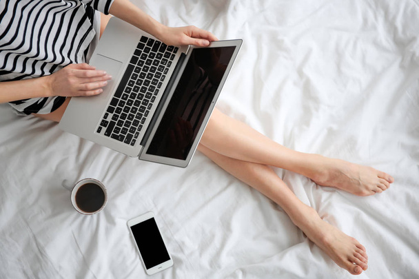 Female blogger with laptop and cup of coffee on bed, top view - Fotó, kép