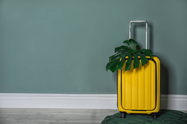 Bright yellow suitcase with tropical leaf near color wall indoors - Фото, изображение