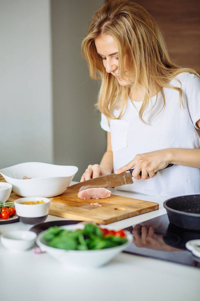 Γυναίκα κοπής chiken κρέας σε ένα τραπέζι κουζίνας με ένα μεγάλο μαχαίρι σεφ - Φωτογραφία, εικόνα
