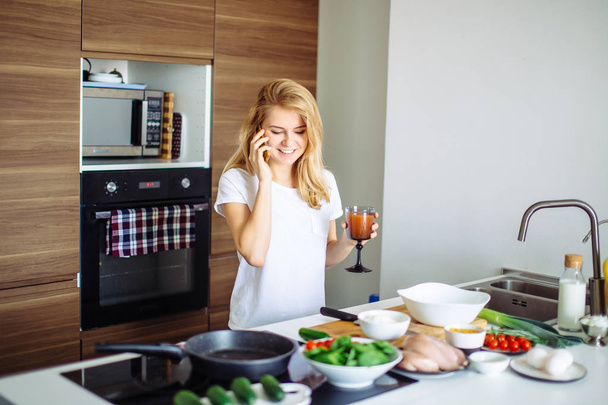 Woman making healthy meal and reading message at phone in the domestic kitchen. - Φωτογραφία, εικόνα