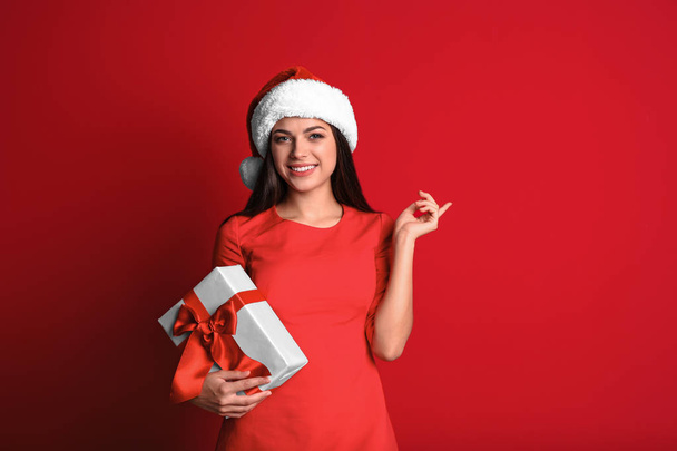 Mulher bonita nova no chapéu de Santa com caixa de presente no fundo da cor. Celebração de Natal
 - Foto, Imagem