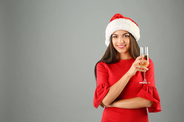 Young beautiful woman in Santa hat with glass of champagne on grey background. Christmas celebration - Foto, imagen